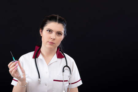 closeup of female nurse with stethoscope and syringe over dark background, vaccination conceptの写真素材