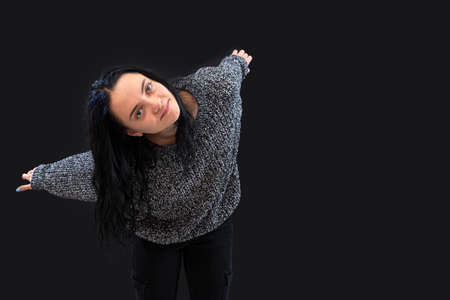 woman with long dark hair wearing gray knitted sweater on a black background  gesticulating with her handsの写真素材