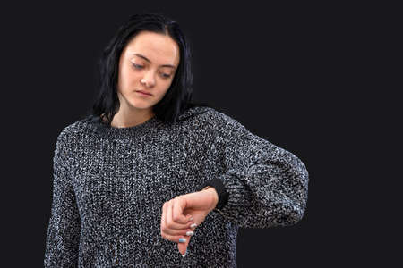 busy female in gray sweather worried looking at her wristwatch, female being late, isolated on blackの写真素材