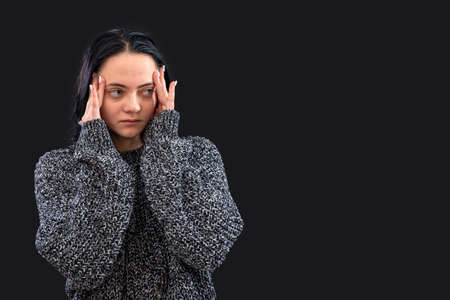 woman with long dark hair wearing gray knitted sweater on a black background  gesticulating with her handsの写真素材