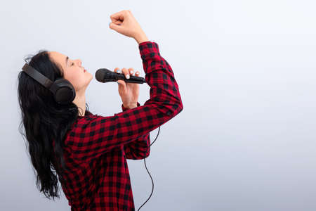 expressive female singing with a microphone and headphones, isolated on light background, mock up,...