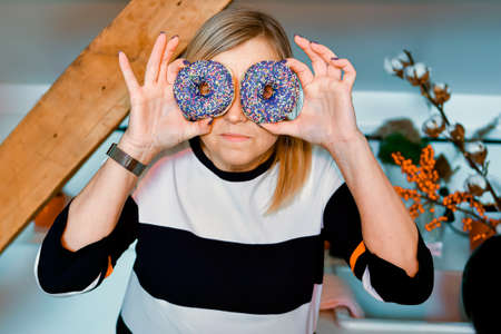 woman holding colorful donuts against her eyes, attractive woman having fun with sweets