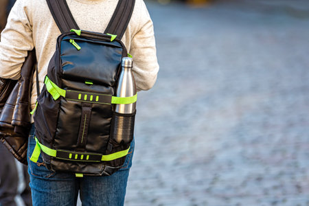 a man with a backpack with a bottle of water from behind on a defocused street background, close-up