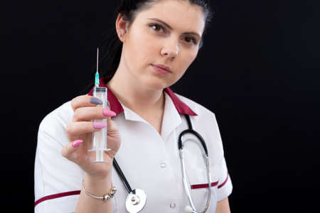 closeup of female nurse with stethoscope and syringe over dark background, vaccination conceptの写真素材