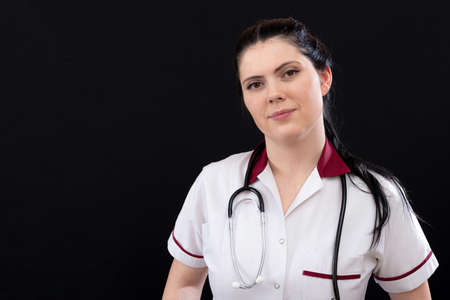 closeup headshot portrait of nurse in uniform with stethoscope, isolated on dark background, copy spaceの写真素材