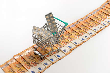 shopping cart full of tablets on the road from fifty-euro banknotes, isolated on white, copy spaceの写真素材