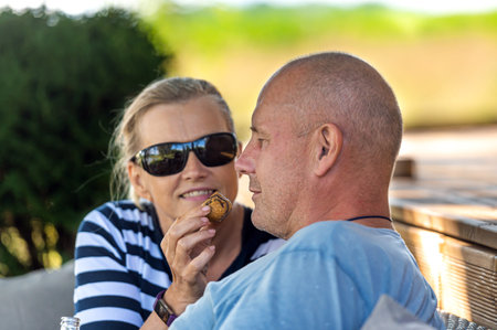 happy married couple feeding one another with cake, engaging outdoor recreation and flirtingの写真素材