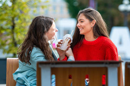 two milenial teenager woman spend free time in outdoor cafe with cocktails, laughing and talking