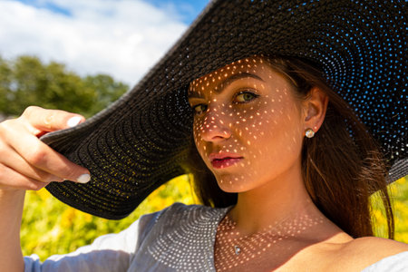 portrait of beautiful sensual brunette in elegant hat, pattern of shadows falling on her faceの写真素材