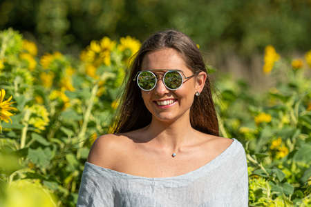 sensual slim woman with long hair in sunglasses in a sunflower field on a sunny summer dayの写真素材