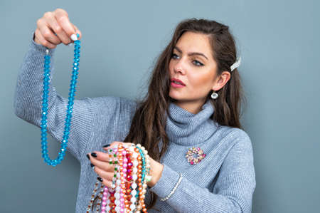slim woman in a long gray sweater has fun with many necklaces bead and jewelry, isolated on grayの写真素材