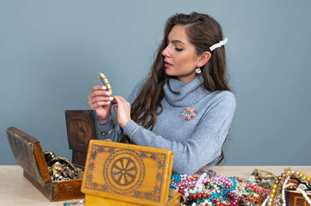 slim brunette sitting at the table with lots of jewelry, choosing and trying different jewelryの写真素材