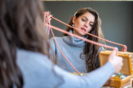 reflection of a woman in mirror choosing and trying different jewelry, soft focus, close-upの写真素材