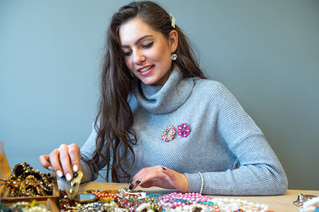 slim brunette sitting at the table with lots of jewelry, choosing and trying different jewelryの写真素材