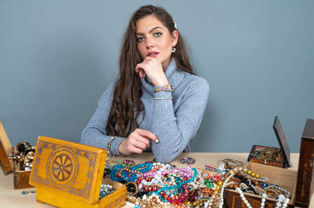 slim brunette sitting at the table with lots of jewelry, choosing and trying different jewelryの写真素材