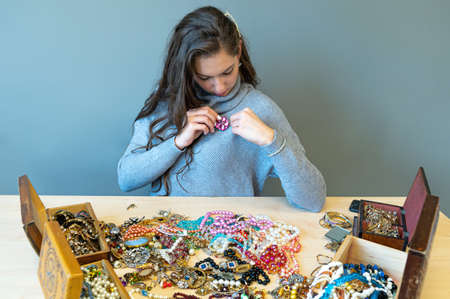 slim brunette sitting at the table with lots of jewelry, choosing and trying different jewelryの写真素材