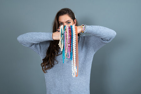 slim woman in a long gray sweater has fun with many necklaces bead and jewelry, isolated on grayの写真素材