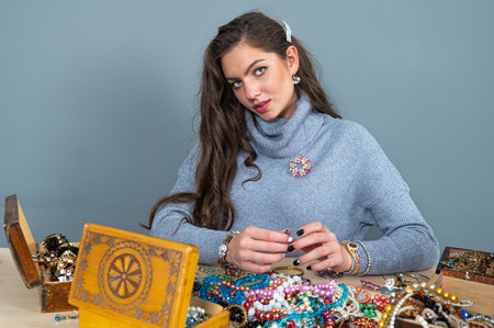 slim brunette sitting at the table with lots of jewelry, choosing and trying different jewelryの写真素材