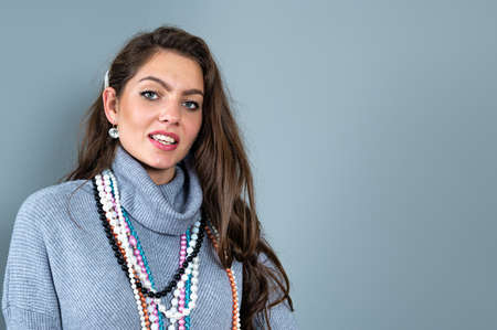 slim woman in a long gray sweater has fun with many necklaces bead and jewelry, isolated on grayの写真素材