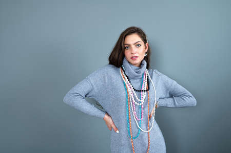 slim woman in a long gray sweater has fun with many necklaces bead and jewelry, isolated on grayの写真素材