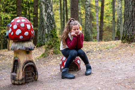 girl sitting on a wooden mushroom sculpture in the woods  in Tervete Nature Park, Latviaの写真素材