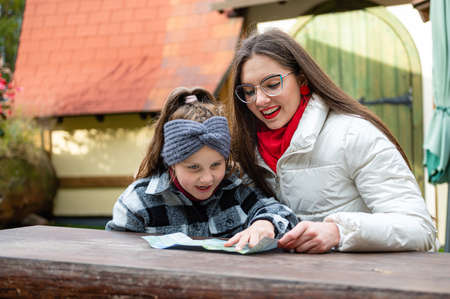 two sisters are sitting at a wooden table in the yard, looking at the map, talking and laughing