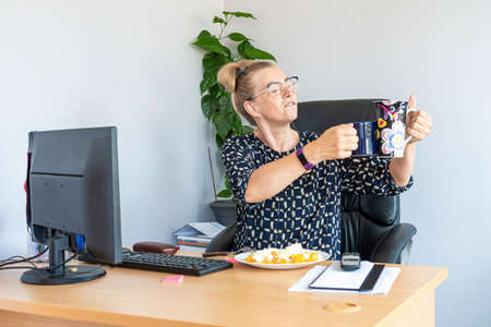 attractive middle-aged woman with eyeglasses at noon in the office at the deskの写真素材