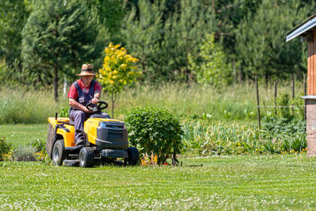 Velena, Latvia - 19 June, 2021: a senior man with a lawn mower mows the grass in the yard of country houseのeditorial素材