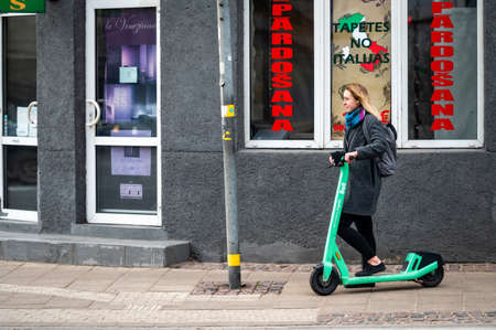 Riga, Latvia, November 2, 2021: a young woman with an electric scooter at a pedestrian crossingのeditorial素材