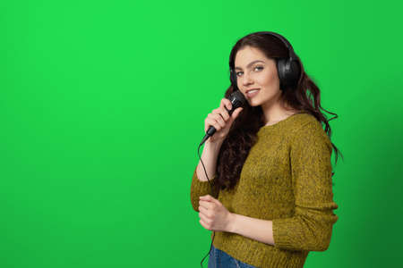 expressive teenager female singing with a microphone and headphones, isolated on green