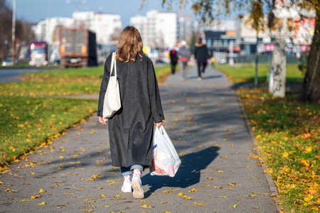 Riga, Latvia, October 29, 2021: woman with shopping bags on a sidewalk in a residential area of the city, rear viewのeditorial素材