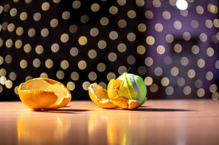 yellow tennis ball in orange peel against a background of bokeh lights, close-upの写真素材