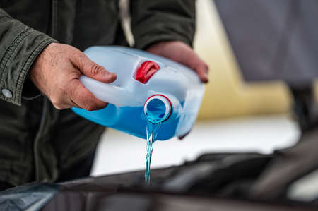 driver refilling the blue non-freezing windshield washer liquid in the tank of the car, closeupの写真素材