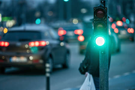 a city crossing with a semaphore on blurred background with cars in the evening streets, green lightの写真素材