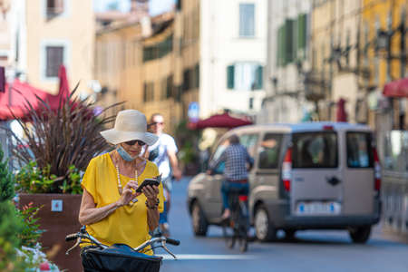 Pisa, Italy - August 9, 2021: a middle-aged woman in a hat and sunglasses is on the street and...