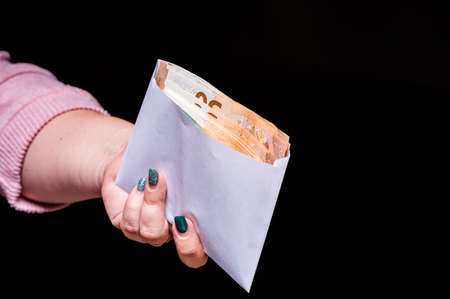 hand holding euro banknotes in the envelope isolated on black background, corruption, bribe, closeupの写真素材