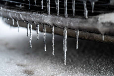 A frozen number plate and Ice-covered car bumper with icicles, closeup