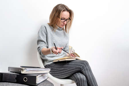 blond woman with glasses counting money and writing in a notebook, isolated on a gray background