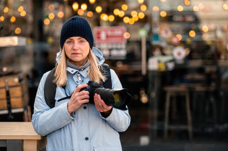 blonde middle-aged woman with a photo camera in the evening on the city streets, lifestyle concept