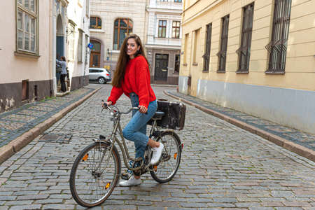 pretty brunette with long hair in a red sweater and jeans on a vintage bike in the old townの写真素材