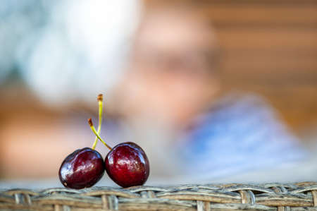 two ripe red cherries on a defocused background, closeup, the concept of a romantic relationshipの写真素材
