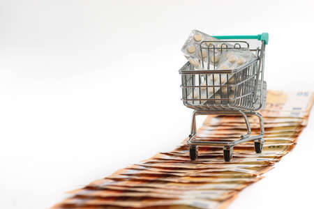 shopping cart full of tablets on the road from fifty-euro banknotes, isolated on white, copy space