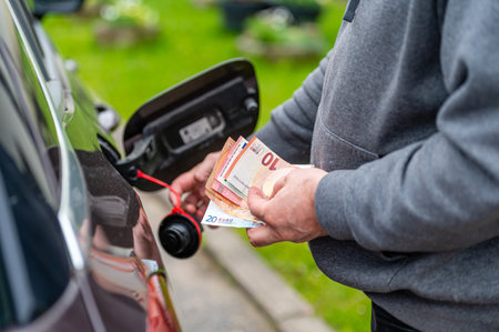 a man s hand counts money while standing at an open fuel tank, the concept of rising fuel pricesの写真素材