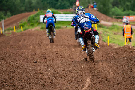 Dobele, Latvia, June 18, 2022: group of motocross riders in action along the dirt road and hilly terrains, view from behindのeditorial素材