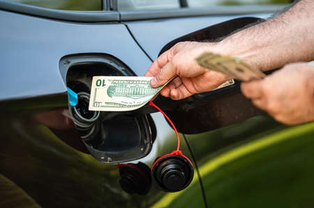 hand of man that puts money into the tank of car, close-up, concept of expensive fuel, fuel crisis