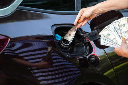 hand of woman that puts money into the tank of car, close-up, concept of expensive fuel, fuel crisisの写真素材