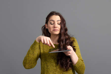 teenage woman with long wavy hair having fun with a tablet, isolated on a gray backgroundの写真素材