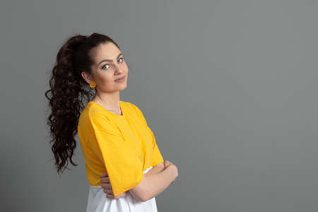 portrait of a young teenager with long wavy hair dressed in a yellow t-shirt, isolated on gray
