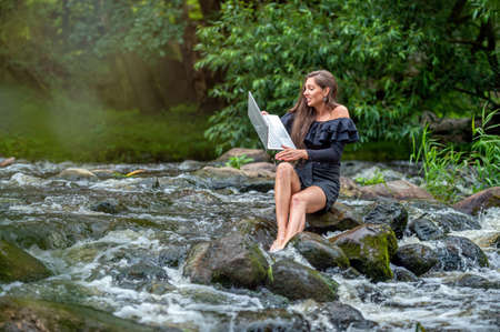 worried woman pulls out of water and rescues laptop that fell into river, holiday work accidentの写真素材