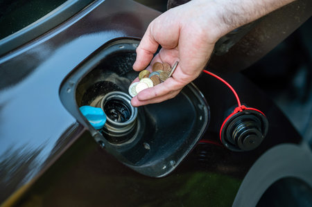 hand of man putting coins in car tank, close-up, expensive fuel concept, fuel crisis